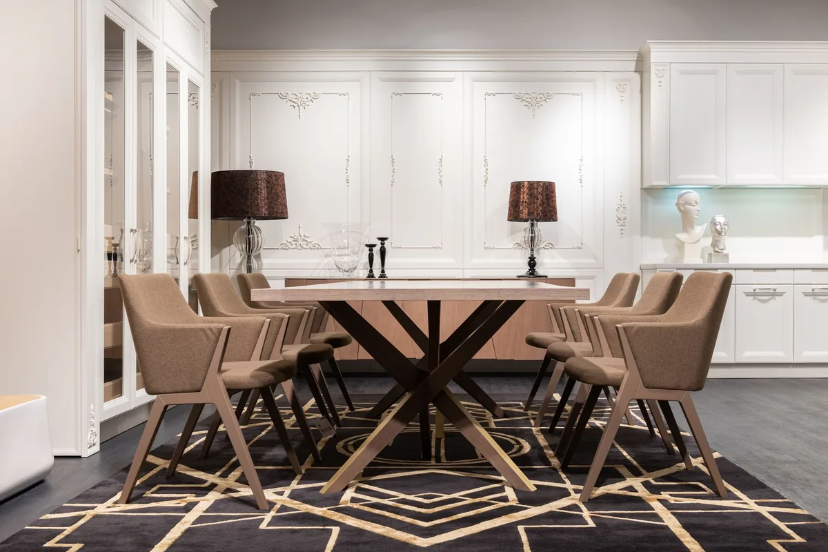 A dining table with upholstered chairs standing on a large dark geometric rug in a white kitchen