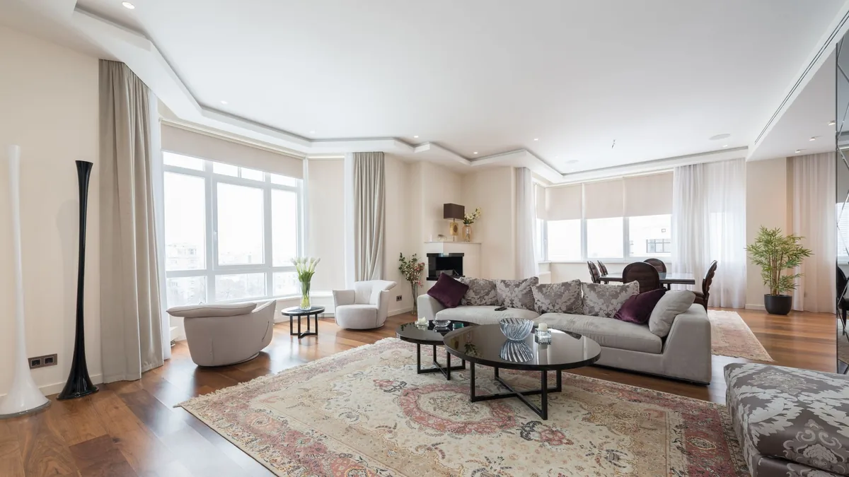 A spacious living room with a grey sofa, two round coffee tables and a large patterned rug on a wood floor