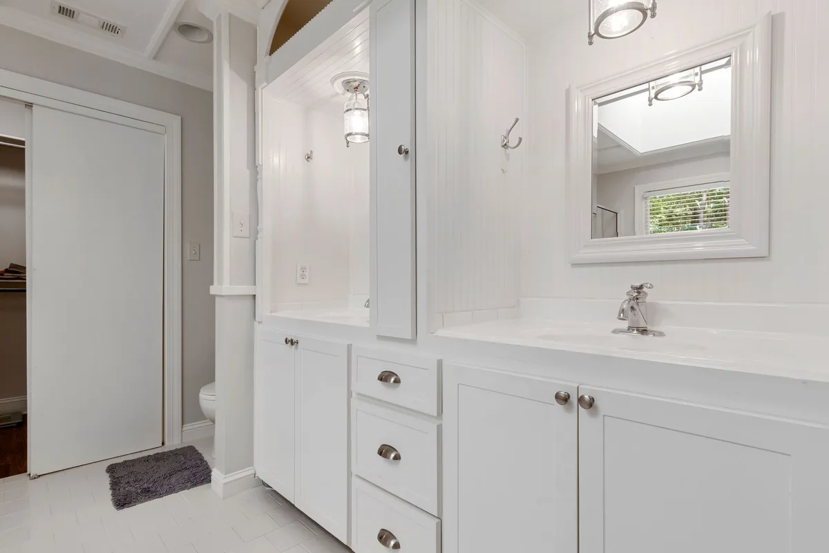 A white vanity with a bank of drawers and doors and a tall wall cabinet beside the mirror