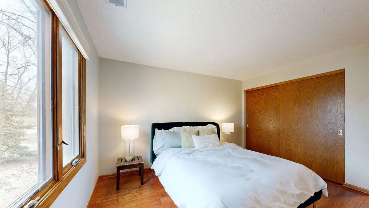 A small bedroom with a made bed, two bedside tables with lamps and a large window