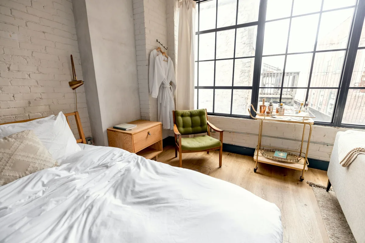 White bed linen on a made bed beside a wooden chair in natural light