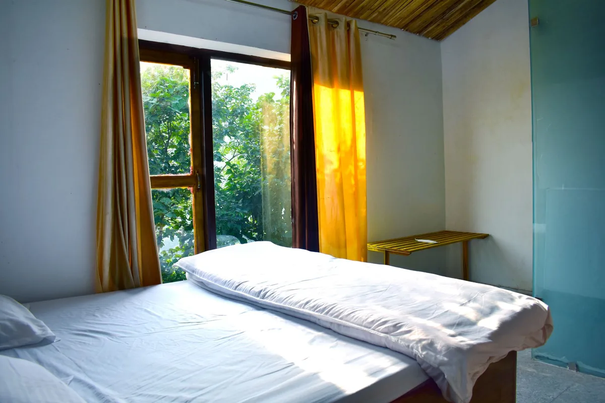A bed beside large windows in a simple, bright bedroom