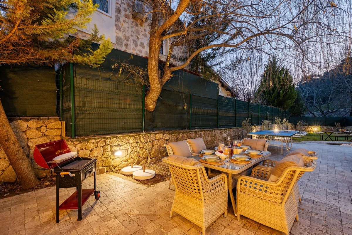 Cream wicker armchairs with cushions around a glass-topped dining table on a stone patio at dusk