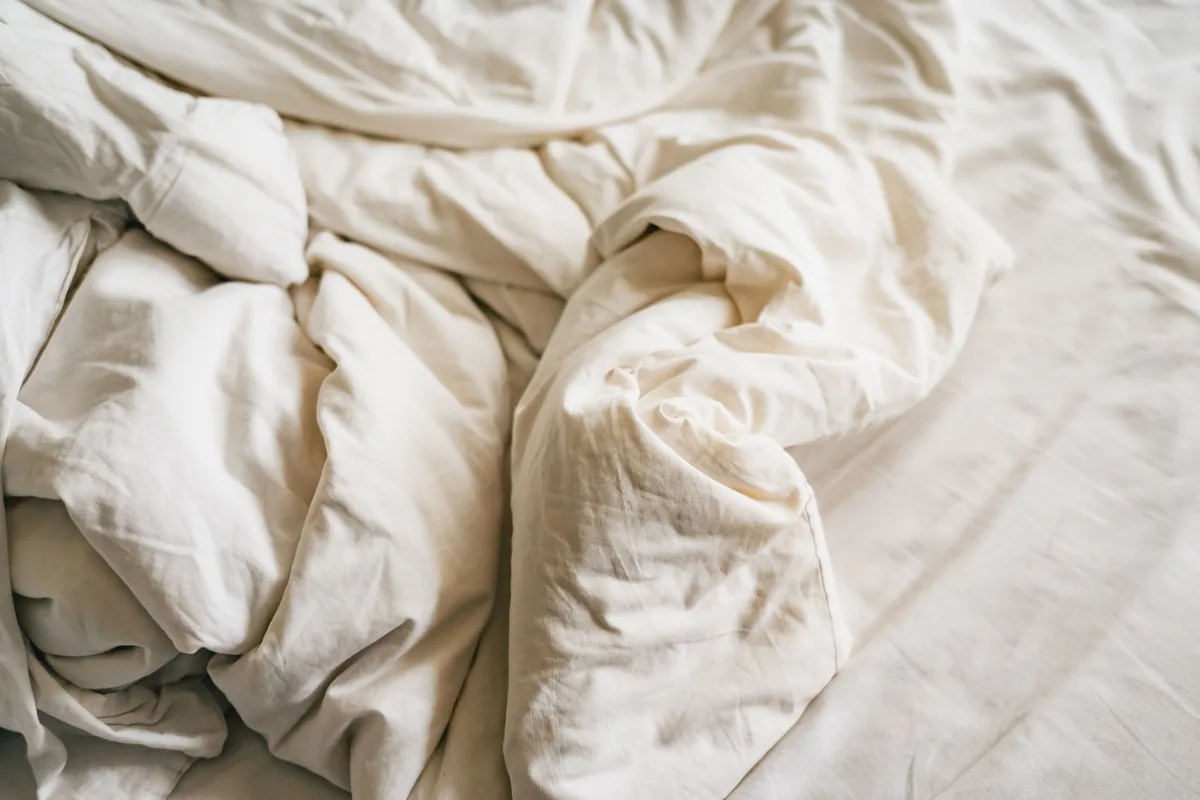 A close-up of rumpled cream bedding on an unmade bed