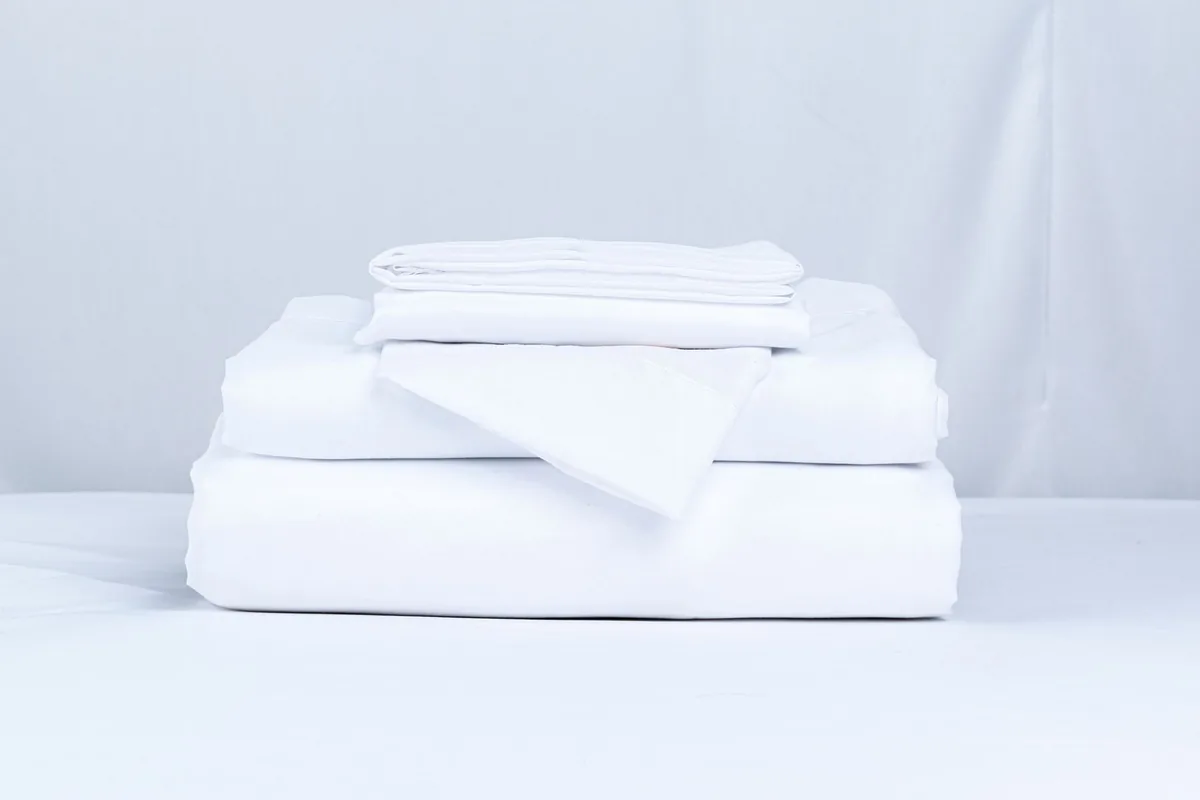 A neatly folded stack of white sheets and pillowcases