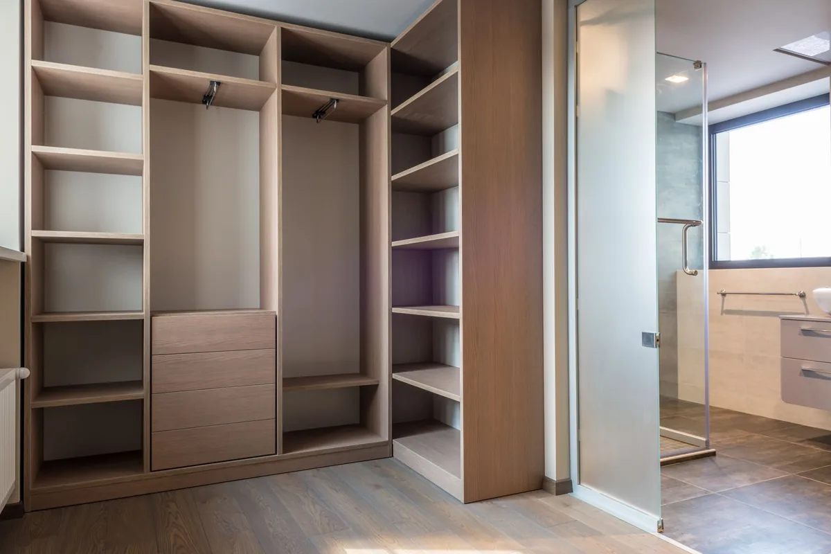 An empty fitted closet with open wooden shelves, two hanging sections and a stack of drawers