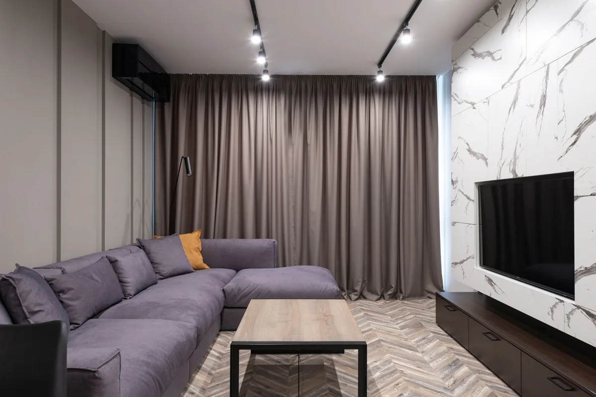 A grey corner sofa with a rectangular wooden coffee table in front of it and a TV unit along the opposite wall