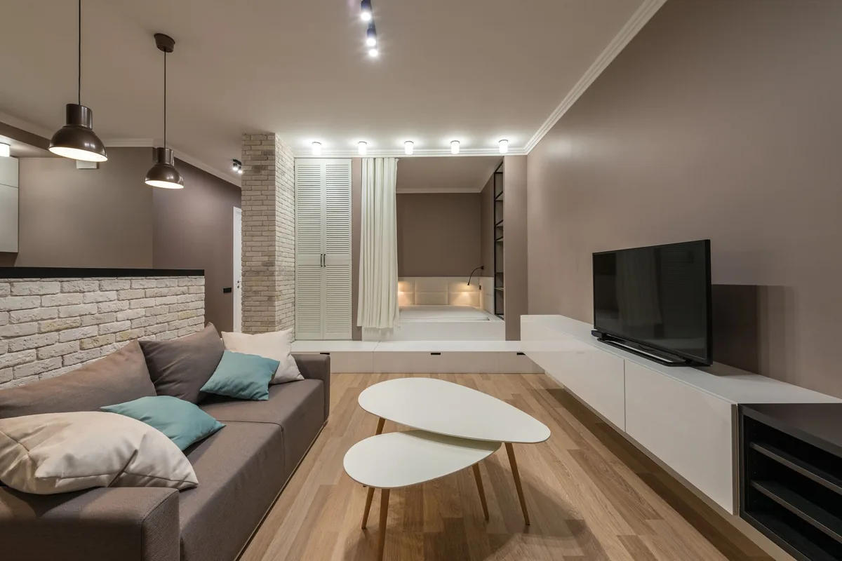 A compact living room with a grey sofa and two white oval nesting tables on a wooden floor