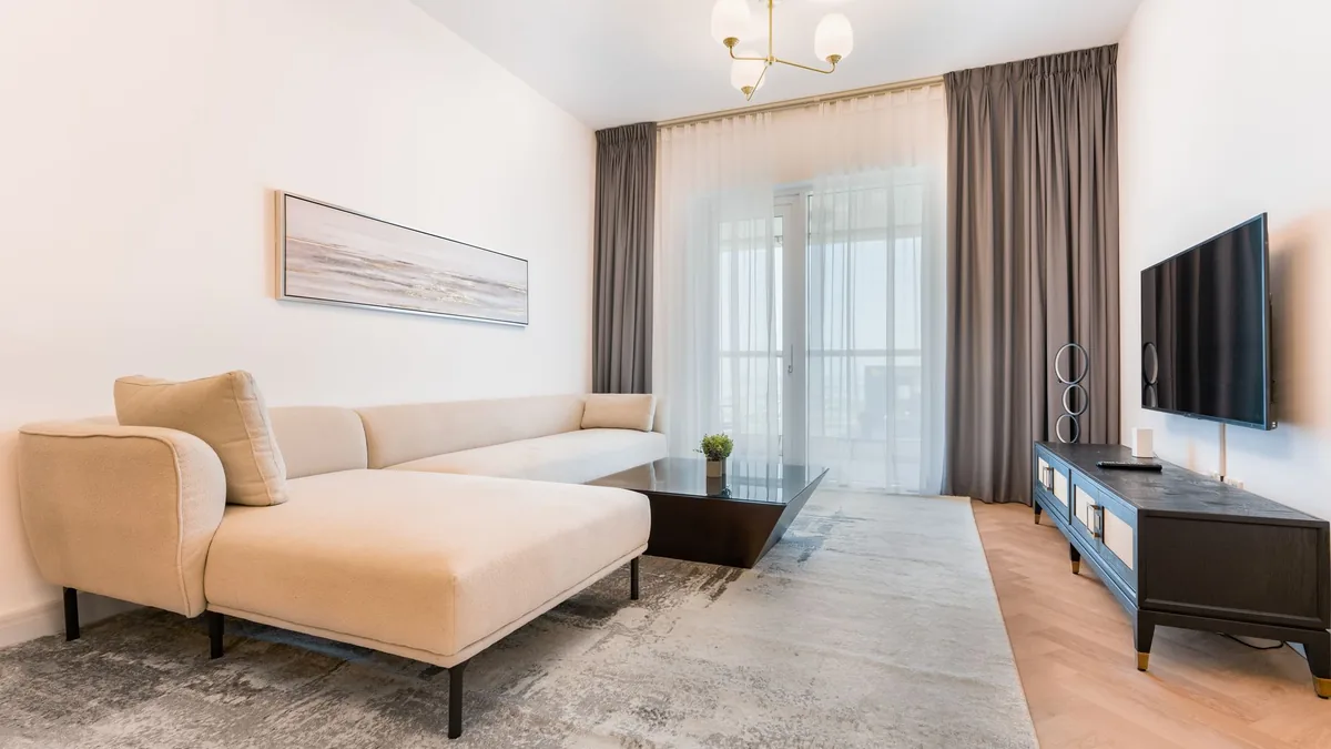 A small living room with a cream chaise sofa, a low dark coffee table on a grey rug and a TV unit opposite