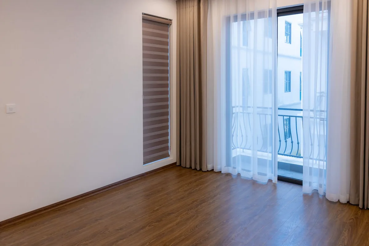 Grey-brown curtains and white sheers falling to a wood floor beside a glass balcony door