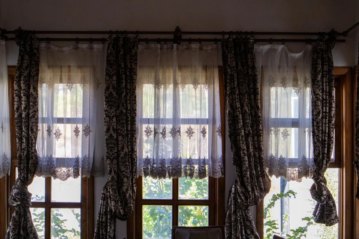 Patterned curtains and lace sheers hanging from rings on a dark metal rod across three windows