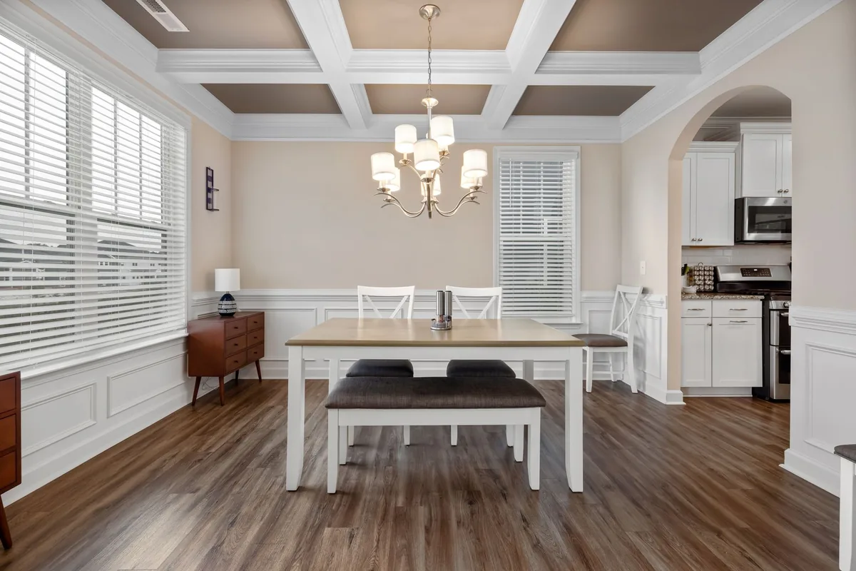 A rectangular dining table with an upholstered bench on one side and chairs on the other, under a chandelier
