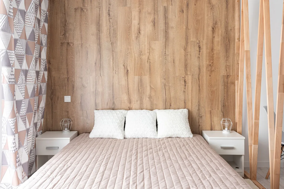 A bed with a pale quilted cover and three white pillows against a wooden wall