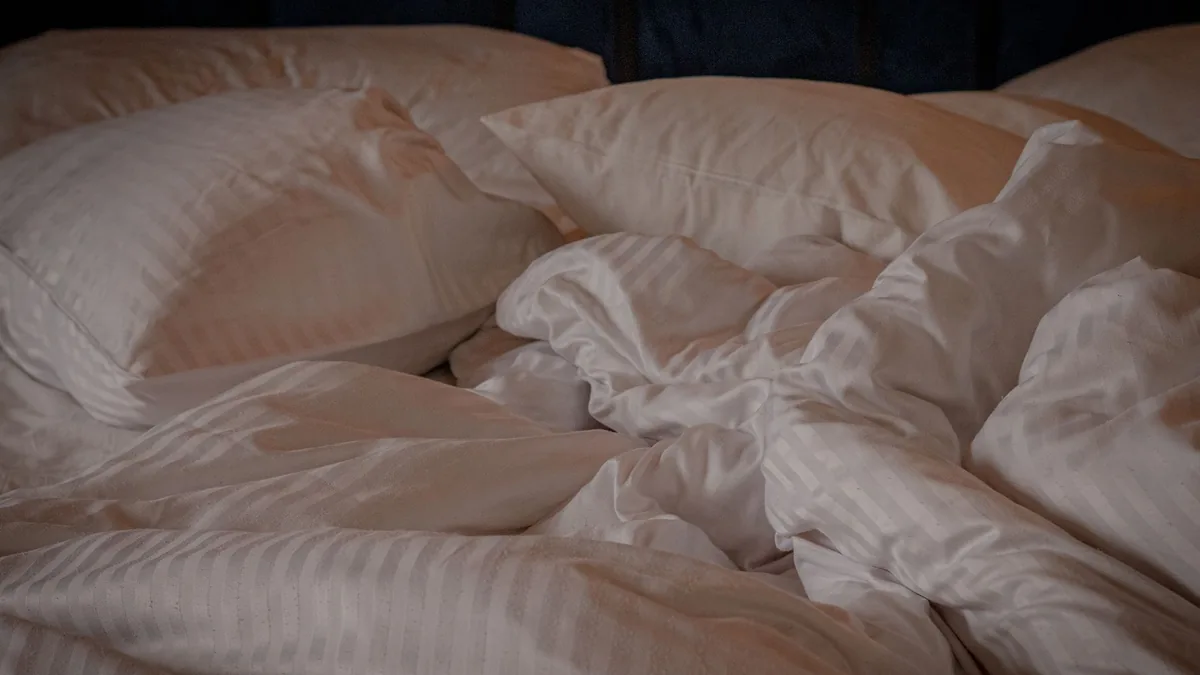 An unmade bed with white striped pillows and a crumpled white duvet