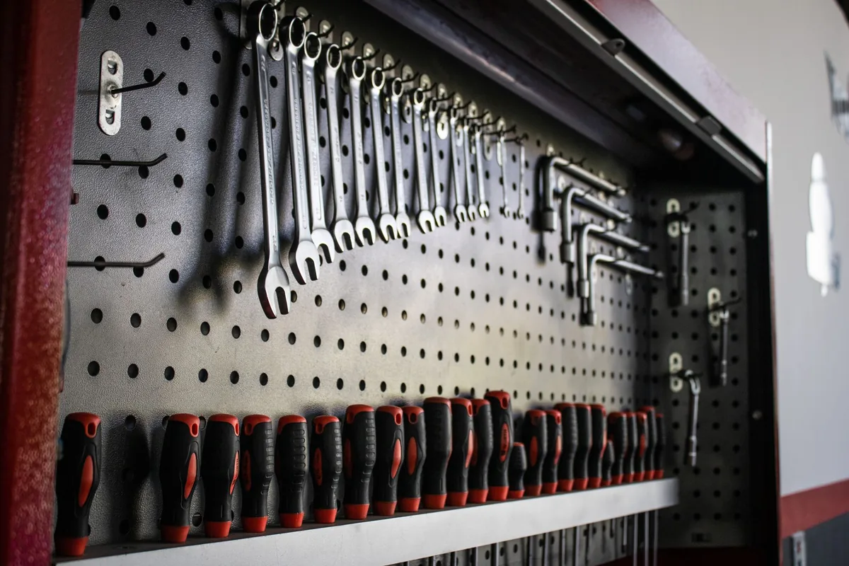 Wrenches and screwdrivers hanging in rows on a dark metal pegboard