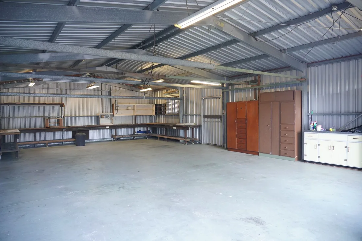 A large empty garage with a workbench along the back wall, two tall wooden cabinets and a row of white base cabinets