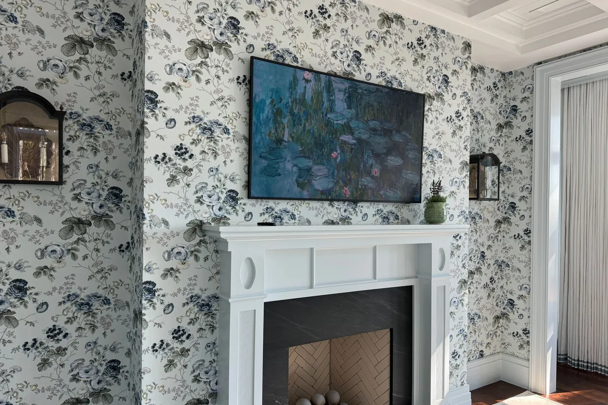 A living room wall covered in blue and gray floral wallpaper above a white fireplace mantel