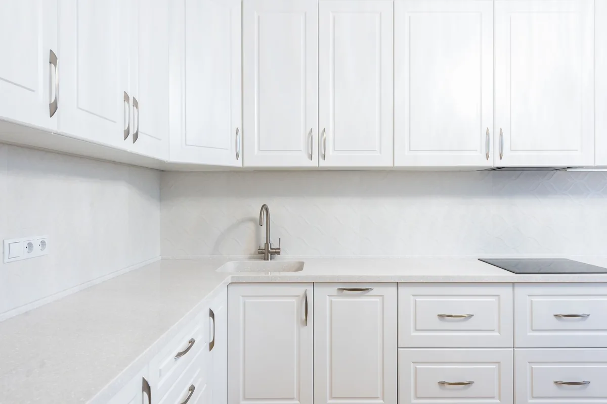 A white kitchen with raised-panel cabinet doors, curved metal pulls and a pale stone countertop