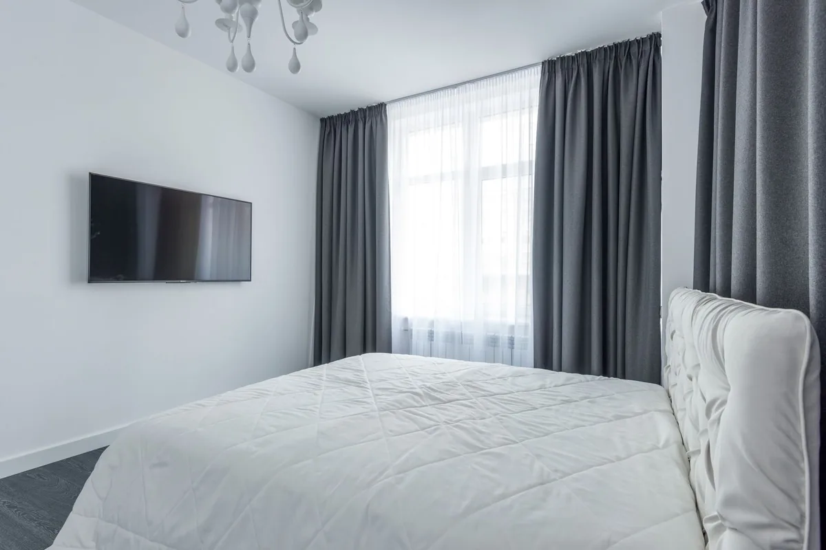 A bedroom window dressed in two layers, white sheer curtains behind floor-length grey drapes