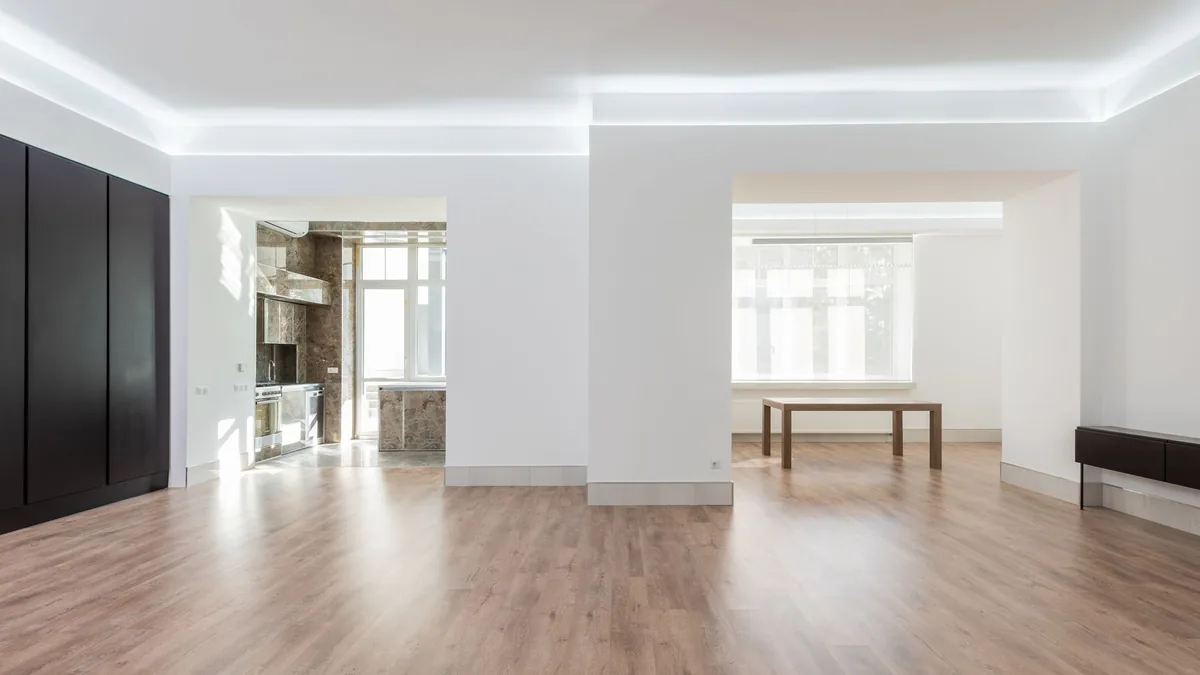 A bright empty room with white walls, wide openings and a light brown wood-look plank floor