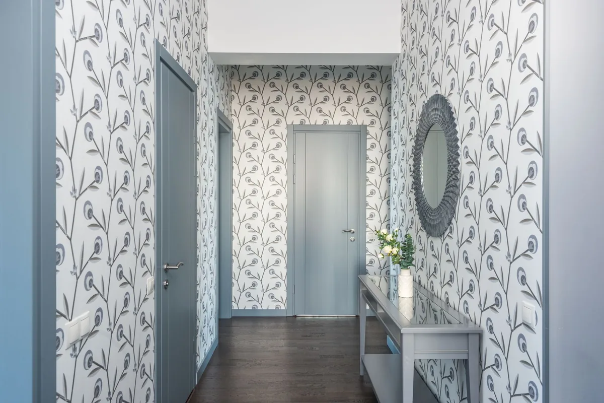 A hallway papered in gray and white botanical wallpaper, trimmed around door frames and a pair of light switches