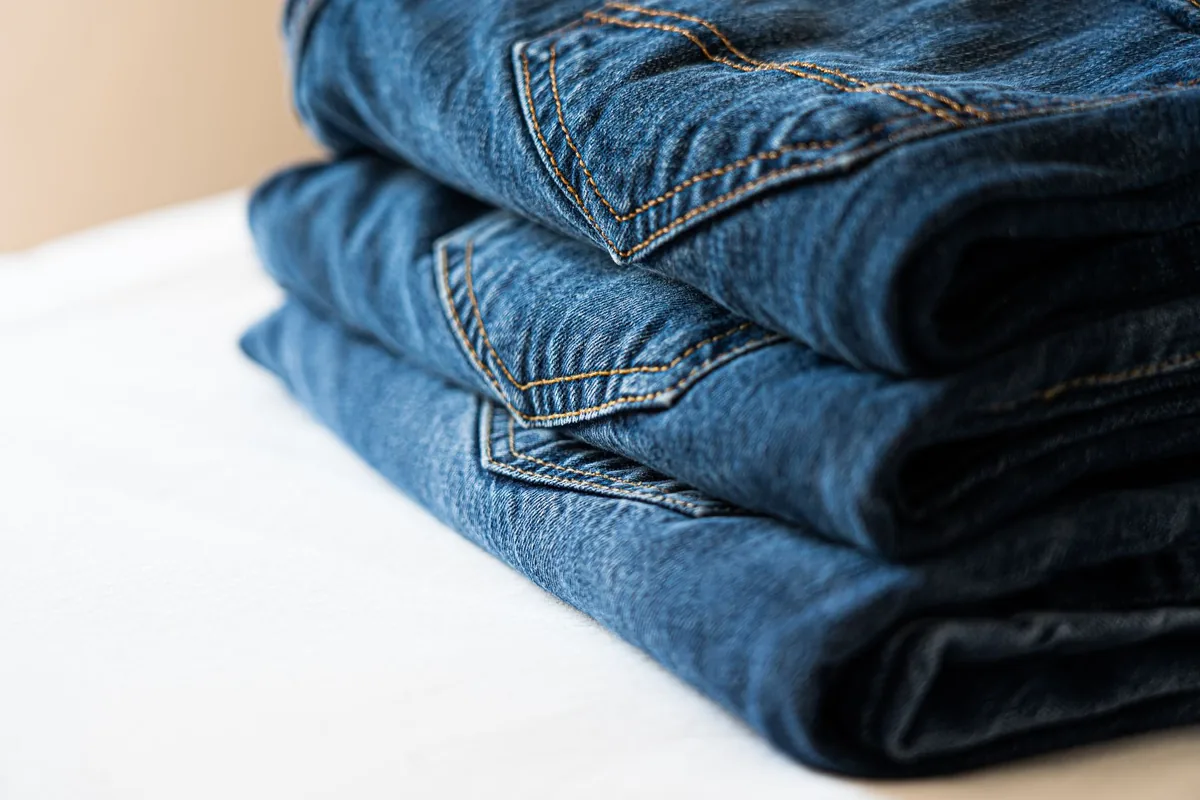 A neat stack of three pairs of folded blue jeans