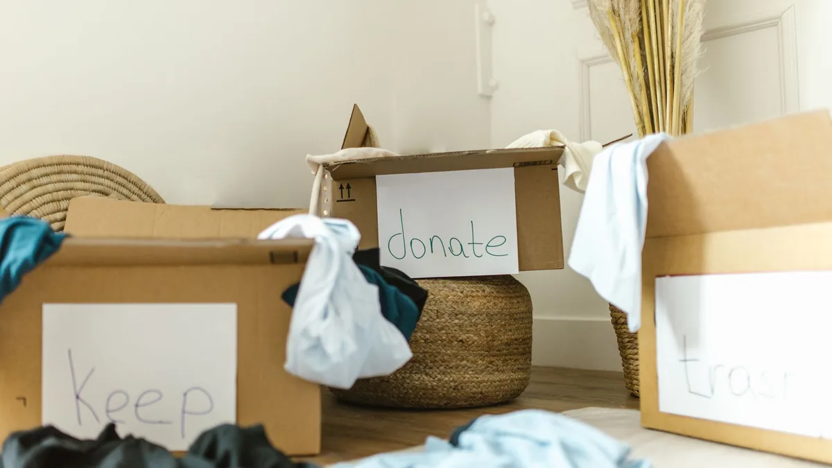 Three cardboard boxes on a floor, hand-labeled keep, donate and trash, with clothes spilling out of them