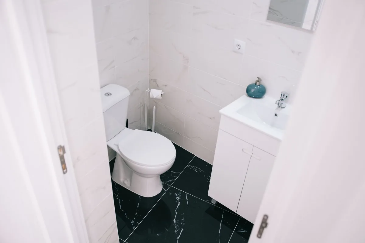 A white floor-mounted toilet on large black marble-look floor tiles in a small bathroom, seen through an open door