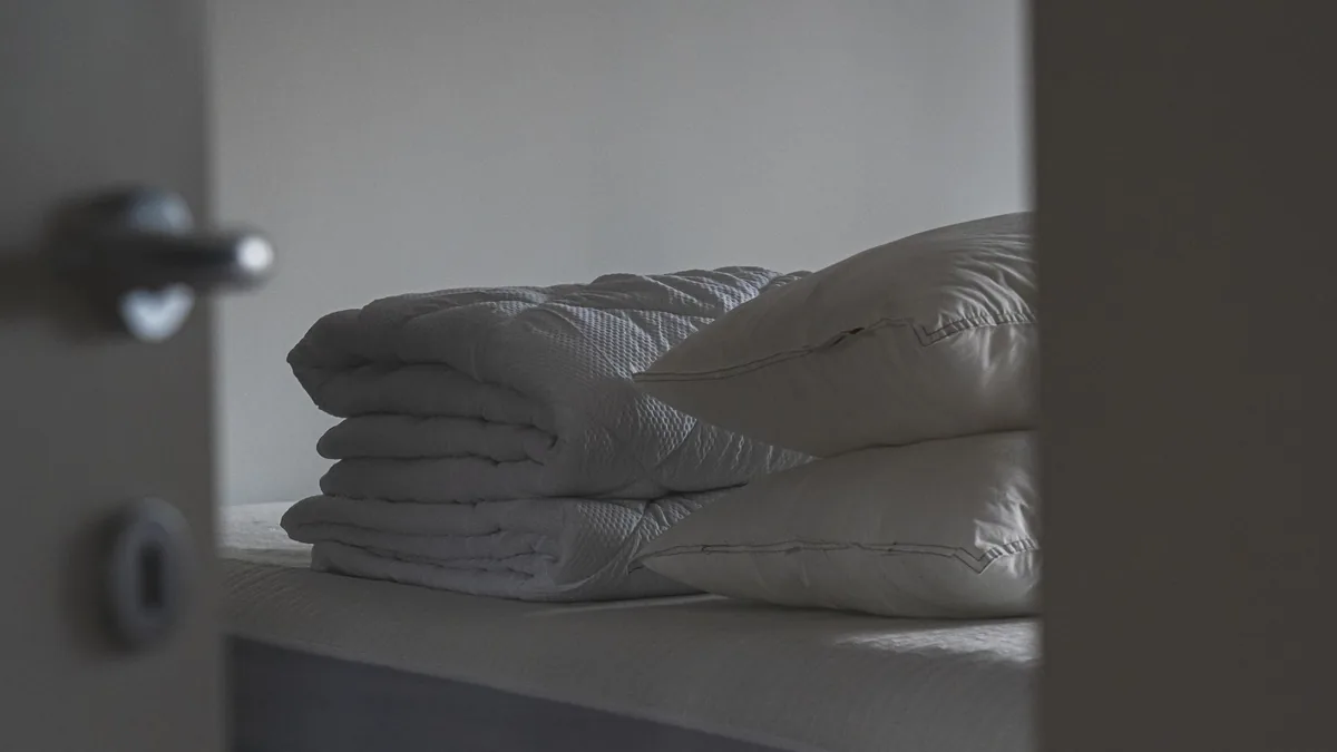 A folded white quilted comforter and two pillows at the end of a bed, seen through a half-open door