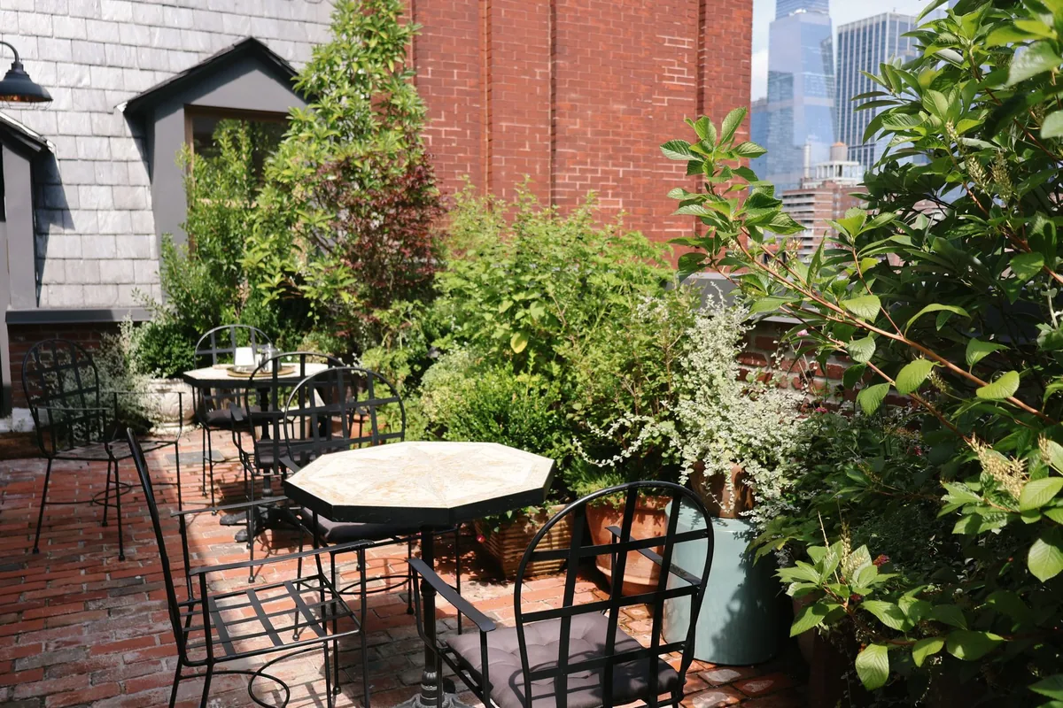 A brick rooftop patio with small tables, black metal chairs and potted plants