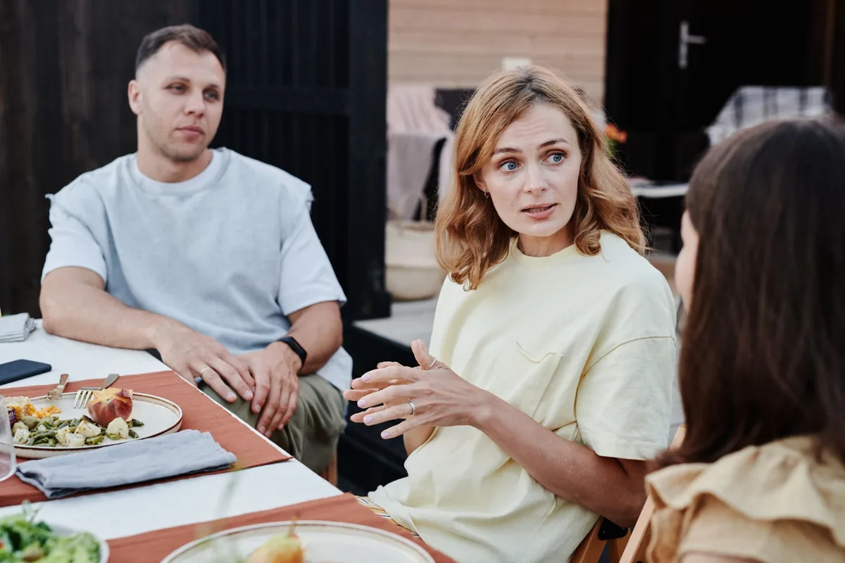 A man and two women seated at a table outdoors, talking over a meal