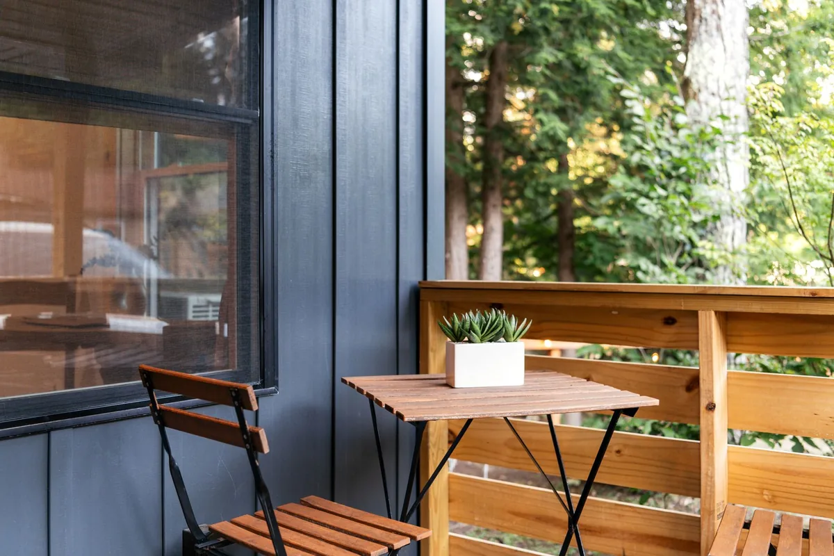 A slatted wooden folding chair and a small folding table with a potted succulent on a narrow deck beside a window
