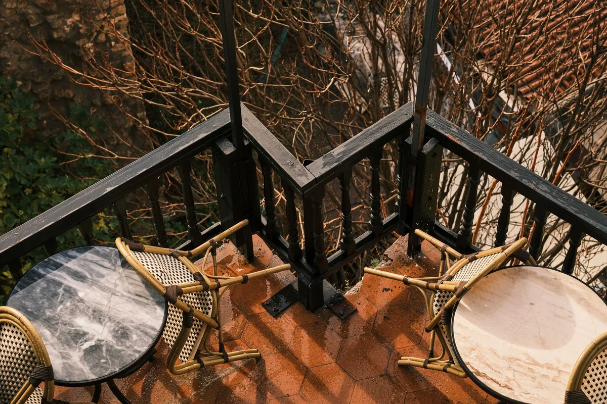 Two small round tables with woven bistro chairs on a balcony with a dark wooden railing, seen from above
