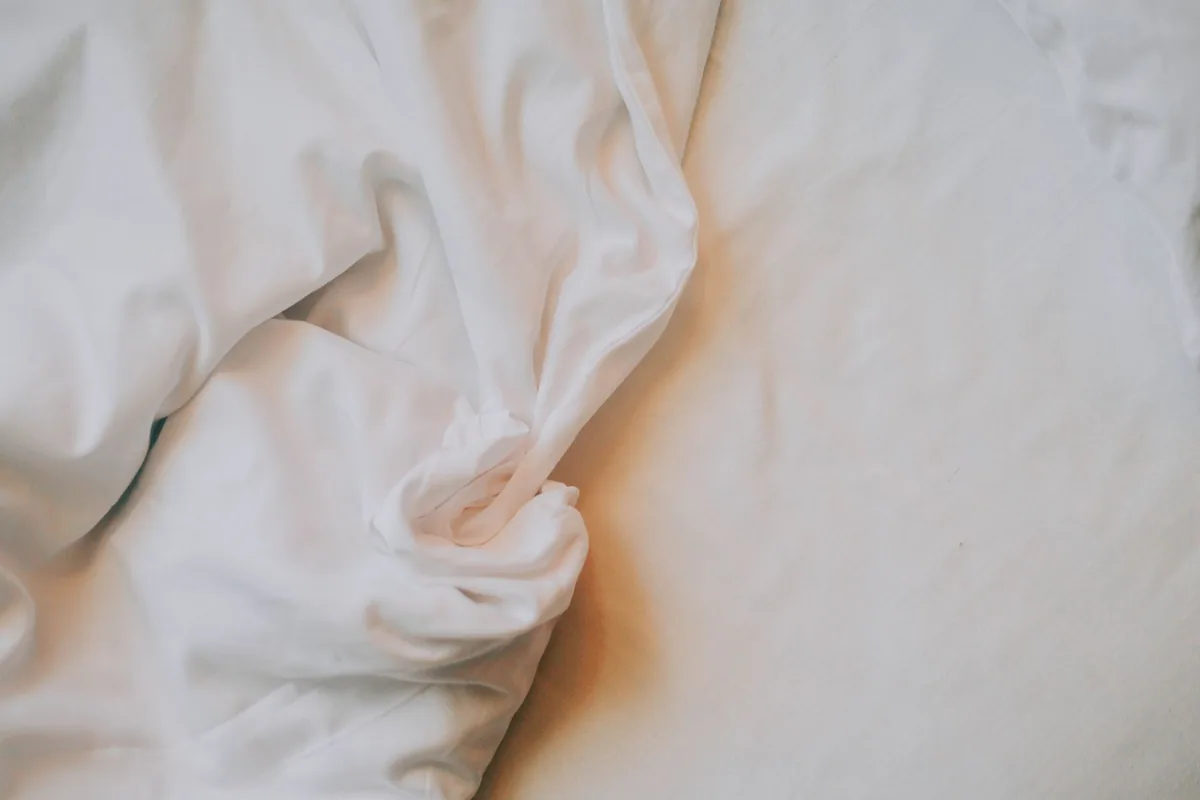A close-up of a crumpled white cotton sheet on a bed