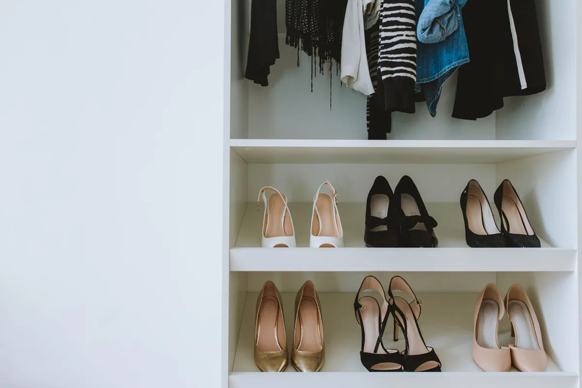 Six pairs of heels lined up three to a shelf in a white closet below hanging clothes
