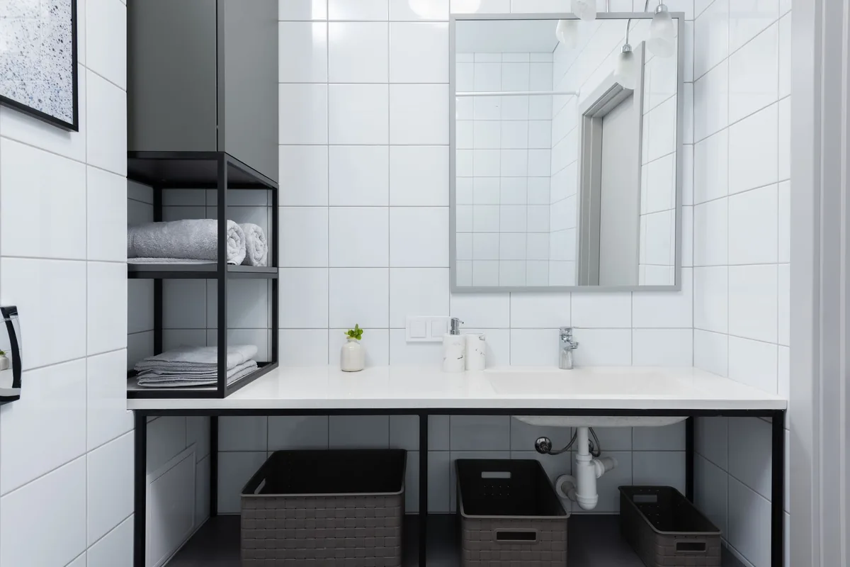 A white tiled bathroom with an open vanity, rolled towels on side shelves and three baskets under the sink
