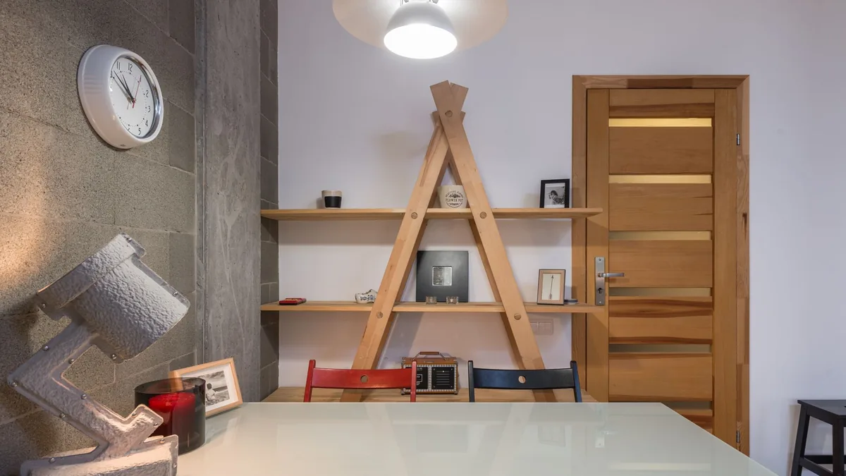 A small dining corner with an A-frame wall shelf, a wall clock and a wooden door