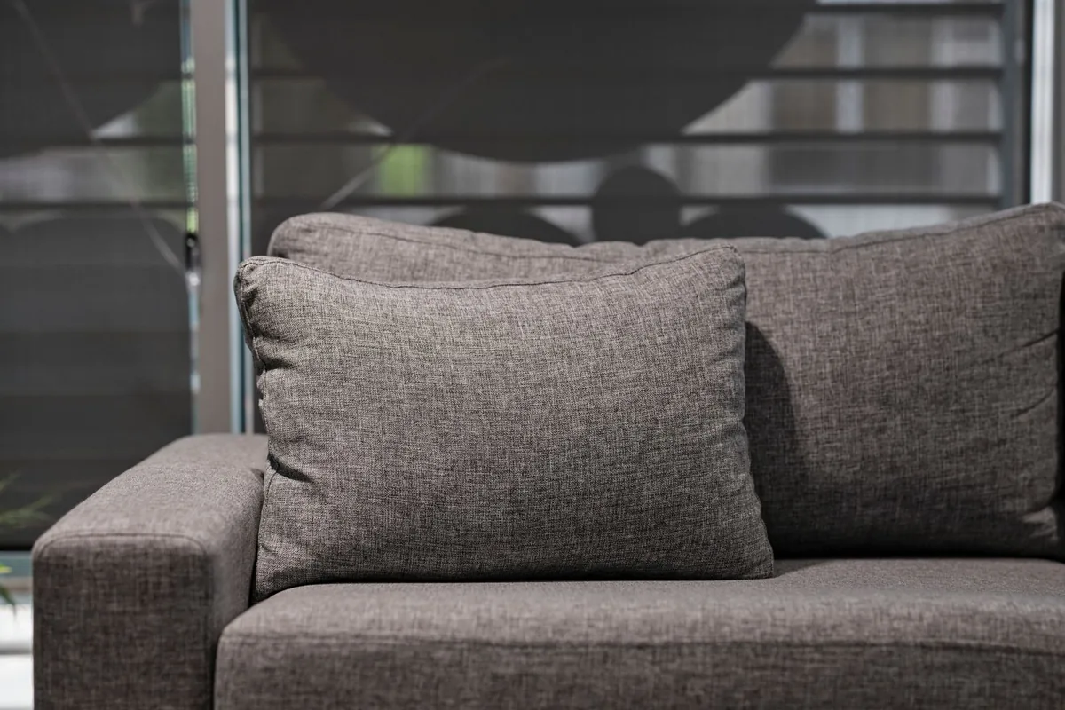 Close-up of a grey upholstered sofa showing a square arm, a seat cushion and a loose back cushion