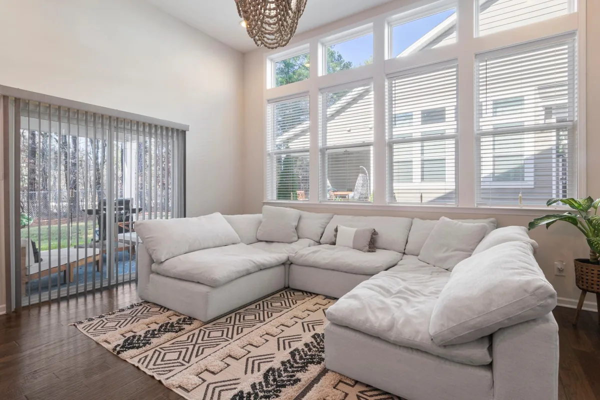 A white modular U-shaped sectional on a patterned rug in a living room with tall windows